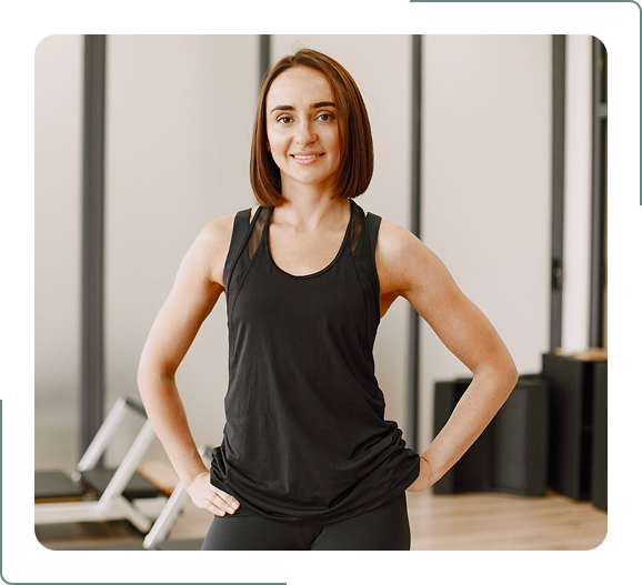 Female fitness trainer standing confidently in gym with hands on hips